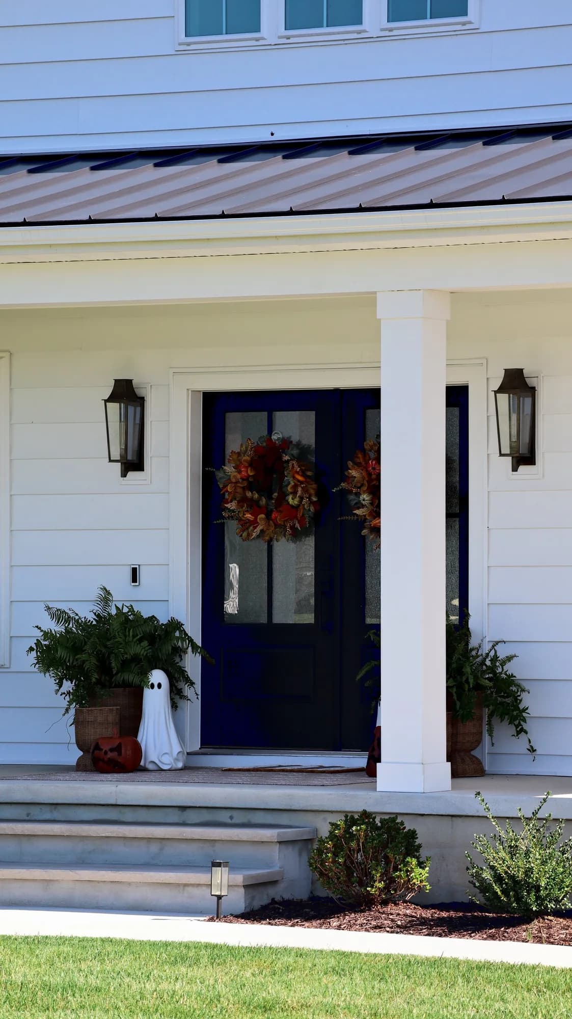 Black double front doors with fall wreaths on the covered porch, between a white column and a carriage lantern