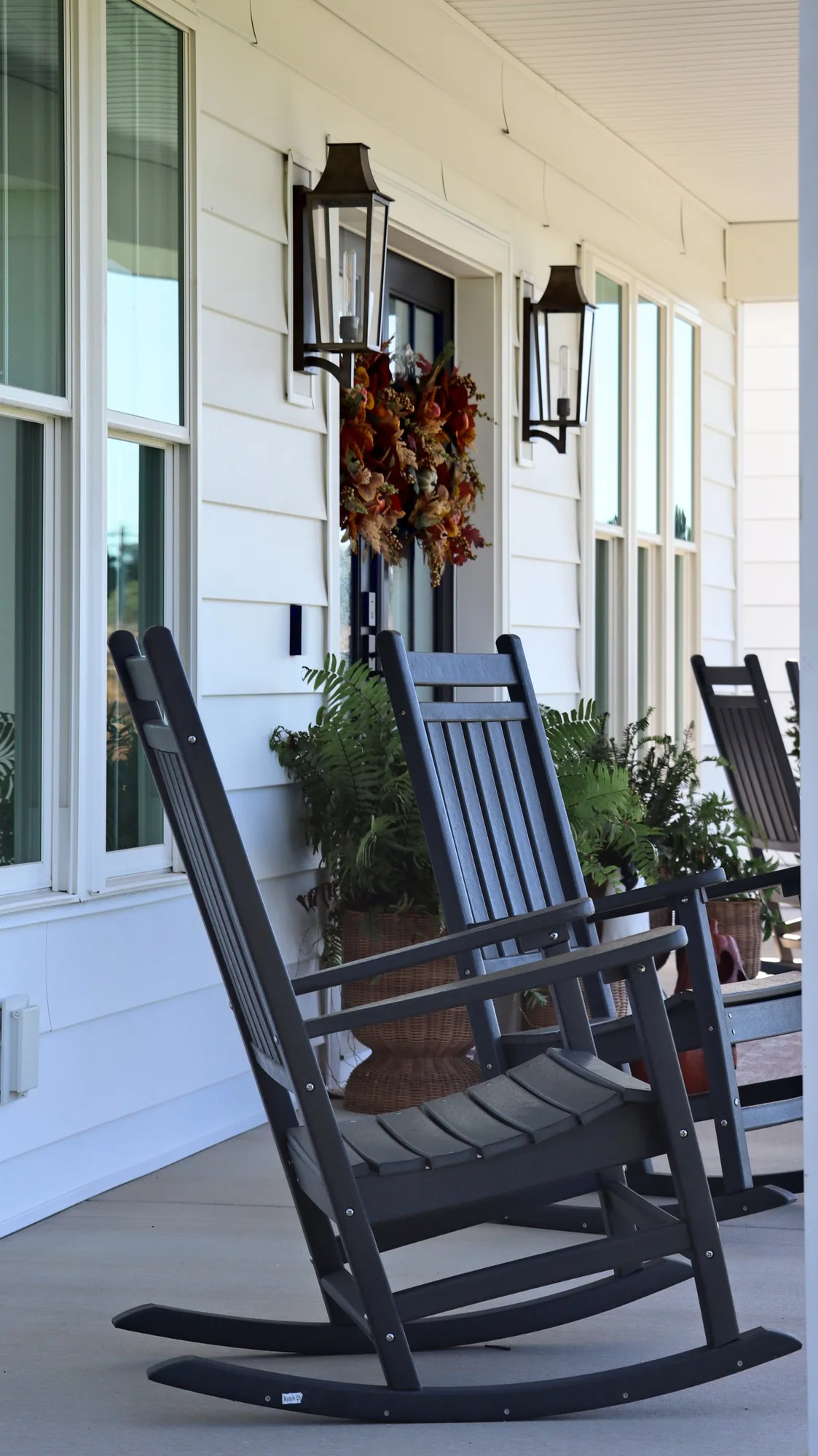A black rocking chair on the front porch beside tall windows and a carriage lantern